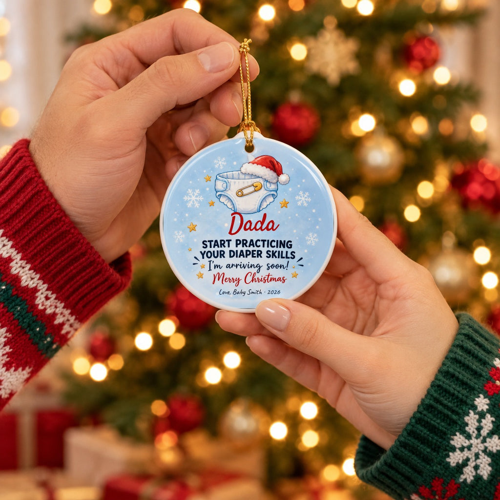 Personalized Daddy, Start Practicing Your Diaper Skills ornament held up as a gift in front of a Christmas tree